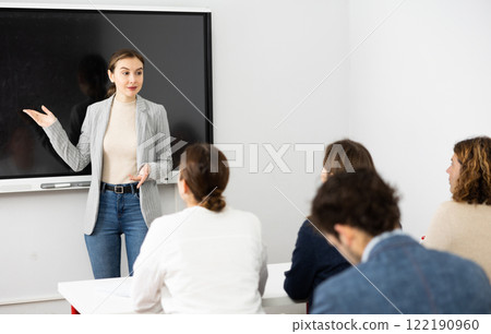 Young female tutor teaching students in college classroom Young female tutor teaching students in college classroom 122190960