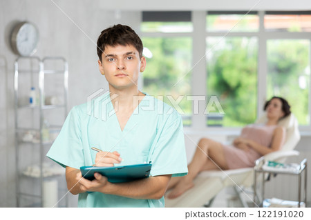 Young man doctor posing in doctor's cabinet with document in hands Young man doctor posing in doctor's cabinet with document in hands 122191020
