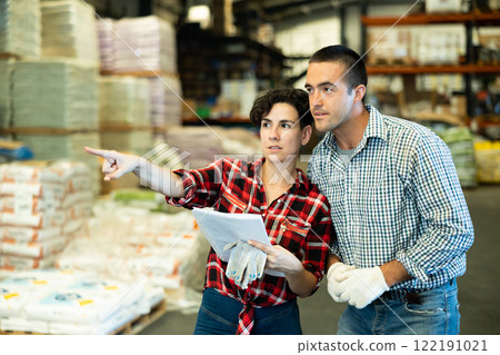 Man and woman working in warehouse, checking documents and poitning finger 122191021