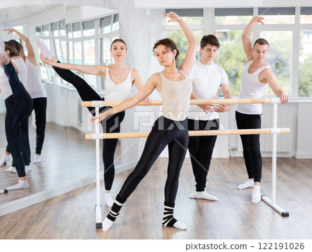 Group of adult students of ballet class posing at barre in studio 122191026