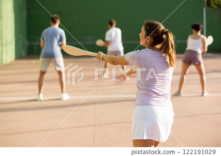 Active womans with enthusiasm playing paleta fronton group on outdoor court 122191029