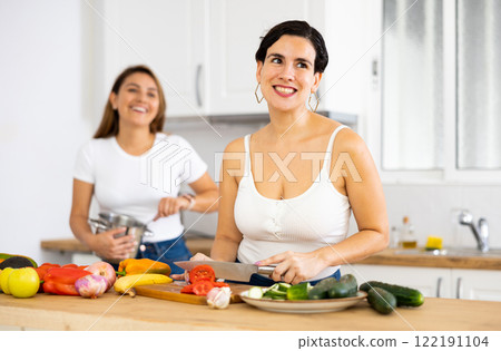 Happy cheerful female friends preparing salad and lunch together in kitchen 122191104