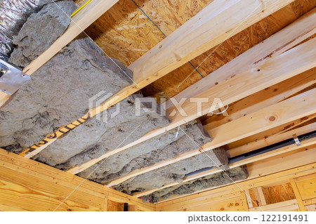 Workers install insulation between wooden beams in building, enhancing energy efficiency, comfort during construction new home 122191491