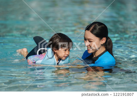 mother teaching toddler baby girl swimming in pool and wearing life jacket 122191807