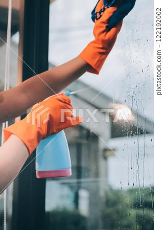 Young female worker cleaning window glass with cloth in spacious villa 122192002