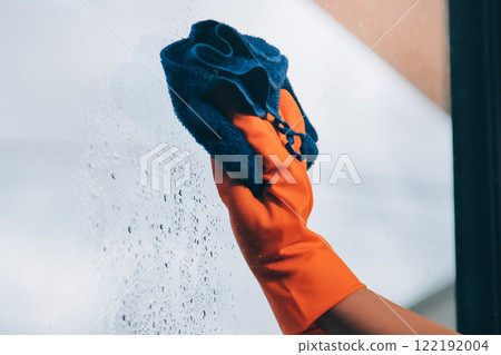 Young female worker cleaning window glass with cloth in spacious villa 122192004