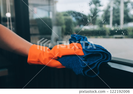 Young female worker cleaning window glass with cloth in spacious villa 122192006