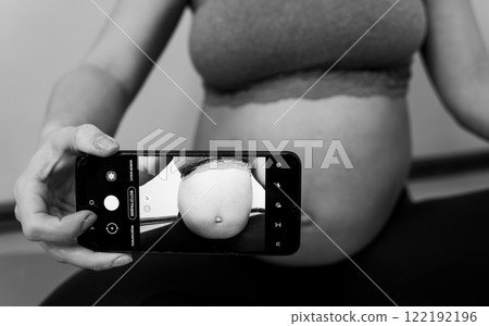 Pregnant woman taking a photo of her belly 122192196