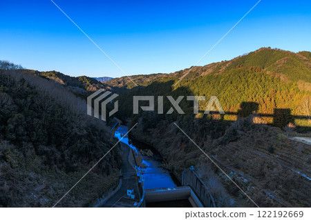 A mild autumn evening at Nunome Dam in Nara during the harsh winter. The Nunome Dam dam casts a shadow on the mountainside surrounding the Nunome River. 122192669