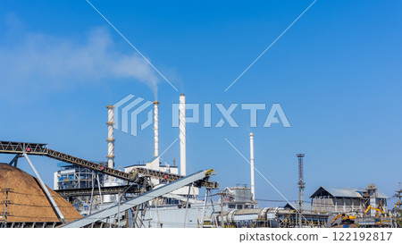 Biomass power plant with wood fuel storage system amidst blue sky. Alternative energy business from plants and wood waste. Renewable energy, Green energy, Recycling and Natural resource conservation. Biomass power plant with wood fuel storage system amidst blue sky. Alternative energy business from plants and wood waste. Renewable energy, Green energy, Recycling and Natural resource conservation. 122192817