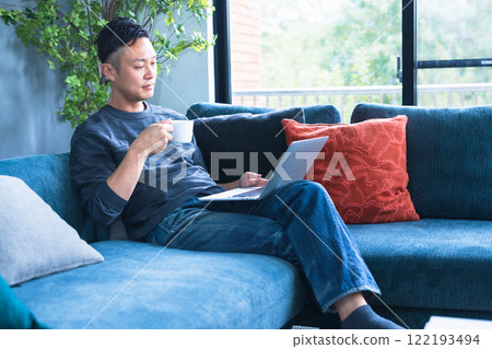 A man sitting on a sofa and using a computer 122193494