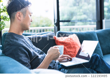 A man sitting on a sofa and using a computer 122193495