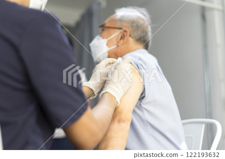 Medical worker perform a vaccine injection to senior Asian man in clinic or medical facility. Medical worker perform a vaccine injection to senior Asian man in clinic or medical facility. 122193632