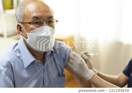 Medical worker perform a vaccine injection to senior Asian man in clinic or medical facility. Medical worker perform a vaccine injection to senior Asian man in clinic or medical facility. 122193639