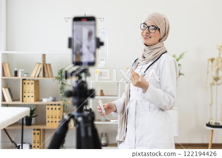 Young Muslim woman wearing hijab records educational medical video on setting up an IV for patient care. She is a healthcare professional using technology to share knowledge online. Young Muslim woman wearing hijab records educational medical video on setting up an IV for patient care. She is a healthcare professional using technology to share knowledge online. 122194426