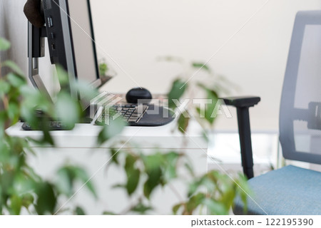 A bright and inviting office setup featuring a computer with accessories on a desk. Green plants in focus add a touch of nature to the contemporary design. Comfortable office seating. 122195390