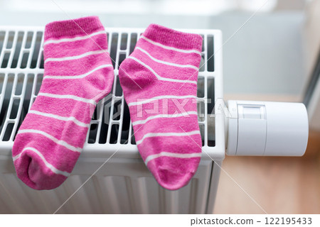 Pink striped socks drying on a home radiator with a modern thermostat. Warmth, domestic comfort, and energy efficiency. 122195433