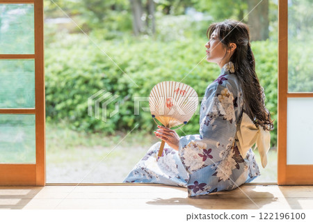 A young woman sitting on the veranda of an old house, cooling off by fanning herself with a paper fan A young woman sitting on the veranda of an old house, cooling off by fanning herself with a paper fan 122196100