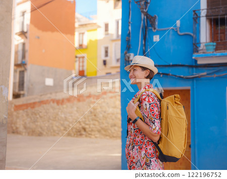 Woman in dress strolls through colorful streets of Spanish coastal town of La Vila Joiosa or Villajoyosa. sunny winter atmosphere highlights charm of Mediterranean architecture and quiet seaside life 122196752