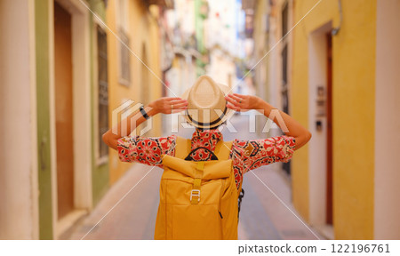 Woman in dress strolls through colorful streets of Spanish coastal town of La Vila Joiosa . sunny winter atmosphere highlights charm of Mediterranean architecture and quiet seaside life, back view 122196761