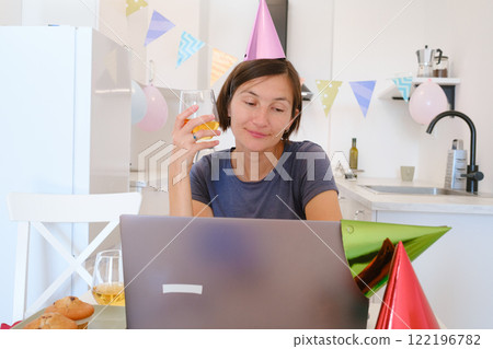 Young woman video chatting with family on her birthday, smiling and joyful as she connects with loved ones from home, celebrating a special day with warmth and connection 122196782