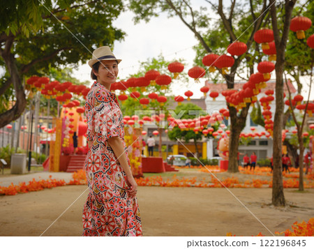 Young woman in ethnic dress and hat exploring the festive streets of George Town, Malaysia, Chinese New Year. Vibrant lanterns, cultural celebrations, and historic charm create a unique atmosphere. 122196845