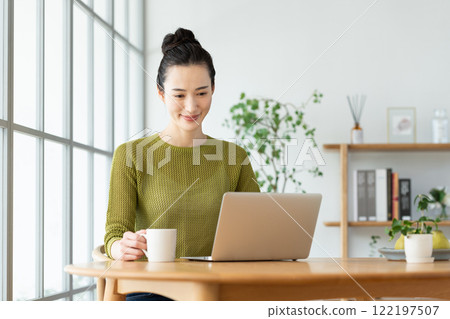 Young woman using a computer while drinking coffee Young woman using a computer while drinking coffee 122197507