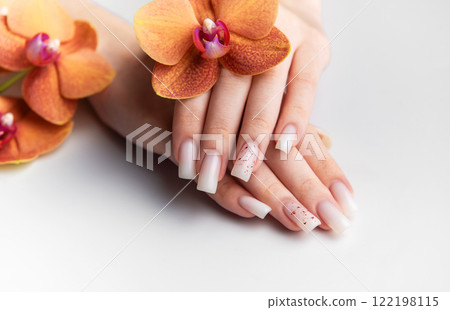 Woman showing stylish white nails with orange orchid decoration 122198115
