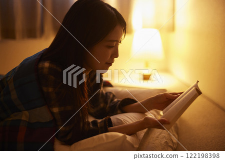 A Japanese woman reading a book under her futon 122198398