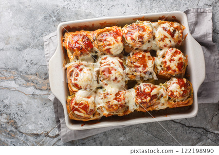Homemade baked sliders stuffed with meatballs, topped with tomato sauce and grated cheese close-up in a baking dish. horizontal top view 122198990