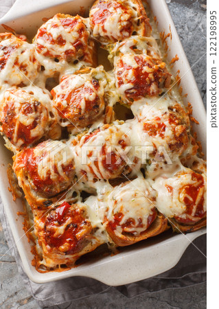 Garlic Bread Meatball Bombs are dinner rolls stuffed with a meatball and sauce, then topped with cheese closeup on the baking dish. Vertical top view 122198995