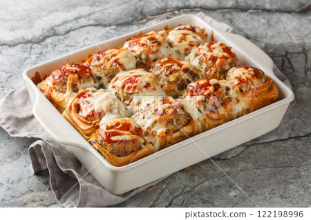 Hot sandwiches made from dinner rolls filled with meatballs, topped with tomato sauce and sprinkled with cheese close-up in a baking dish. horizontal 122198996