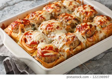 Baked dinner rolls stuffed with meatballs, topped with tomato sauce and sprinkled with cheese close-up in a baking dish. horizontal Baked dinner rolls stuffed with meatballs, topped with tomato sauce and sprinkled with cheese close-up in a baking dish. horizontal 122198997