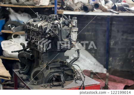 Dismantled car engine placed on a wooden pallet inside a garage environment Dismantled car engine placed on a wooden pallet inside a garage environment 122199014