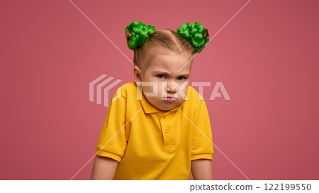 Little girl with a pouty face, arms crossed, wearing yellow shirt and green braided buns against pink studio background. Little girl with a pouty face, arms crossed, wearing yellow shirt and green braided buns against pink studio background. 122199550