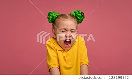 Child, pretty girl in yellow shirt and bun hairstyle standing with mouth open and eyes closed, expressing shock and emotions against pink studio background. Child, pretty girl in yellow shirt and bun hairstyle standing with mouth open and eyes closed, expressing shock and emotions against pink studio background. 122199552