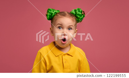 Little girl with astonished expression, mouth open in surprise, wearing yellow shirt and green braided buns against pink studio background. Little girl with astonished expression, mouth open in surprise, wearing yellow shirt and green braided buns against pink studio background. 122199555