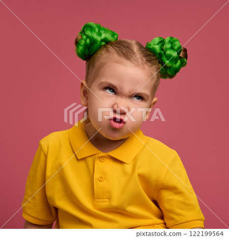Kid, girl with annoyed expression, green braided buns hairstyle, wearing yellow shirt, against pink studio background. Kid, girl with annoyed expression, green braided buns hairstyle, wearing yellow shirt, against pink studio background. 122199564