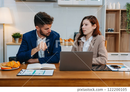 Business documents at kitchen modern office table with tablet and laptop computer and chart and two colleagues working a project or reviewing and discussing a business project. Business documents at kitchen modern office table with tablet and laptop computer and chart and two colleagues working a project or reviewing and discussing a business project. 122200105