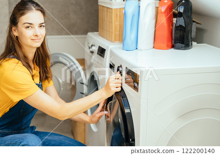 Beautiful young woman housewife doing housework, using washing machine at home laundry. Everyday domestic life, highlighting productivity and routine activities in a stylish and functional interior. Beautiful young woman housewife doing housework, using washing machine at home laundry. Everyday domestic life, highlighting productivity and routine activities in a stylish and functional interior. 122200140