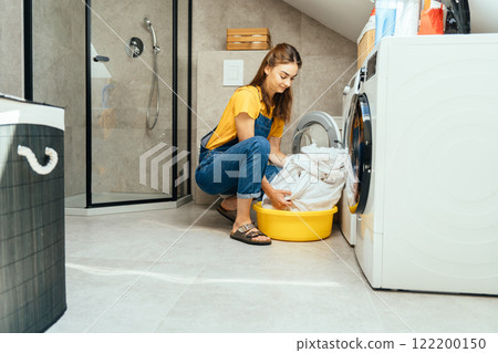 Sorting laundry before washing. A happy young housewife takes out or puts bed linen into the washing machine in a modern minimalist interior. Sorting laundry before washing. A happy young housewife takes out or puts bed linen into the washing machine in a modern minimalist interior. 122200150