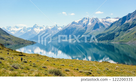 Hikers enjoying breathtaking mountain scenery clear blue lake towering snow covered peaks green meadows. trekking nature walks beautiful landscape environment wilderness alpine travel activity 122200335