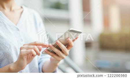 Person using smartphone outdoors, close-up hands holding mobile device, casual clothing, modern technology, communication, touchscreen, digital lifestyle, connectivity, browsing internet, texting Person using smartphone outdoors, close-up hands holding mobile device, casual clothing, modern technology, communication, touchscreen, digital lifestyle, connectivity, browsing internet, texting 122200360