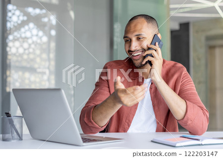 A cheerful professional engages in a phone call while working remotely with a laptop, showcasing modern work flexibility and collaboration. A cheerful professional engages in a phone call while working remotely with a laptop, showcasing modern work flexibility and collaboration. 122203147