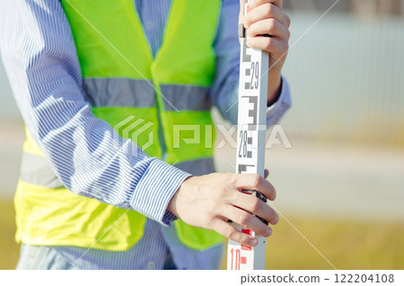 Worker is unfolding leveling rod on construction site. 122204108