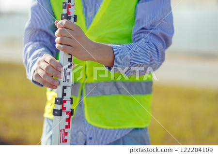 Worker is unfolding leveling rod on construction site. 122204109
