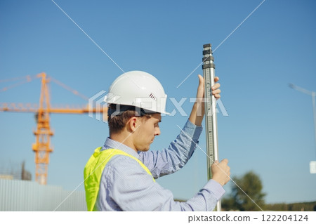 Worker is unfolding leveling rod on construction site. Worker is unfolding leveling rod on construction site. 122204124