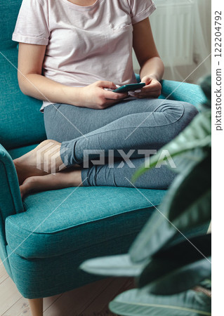 Young woman using mobile phone while sitting in cozy armchair 122204792