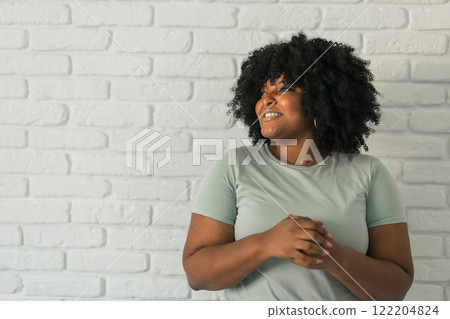 Happy stylish African American young woman with Afro hair laughing looking away standing against white brick wall background copy space. Happy stylish African American young woman with Afro hair laughing looking away standing against white brick wall background copy space. 122204824