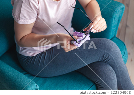 Young woman cleaning glasses with a napkin while sitting in a ch 122204968